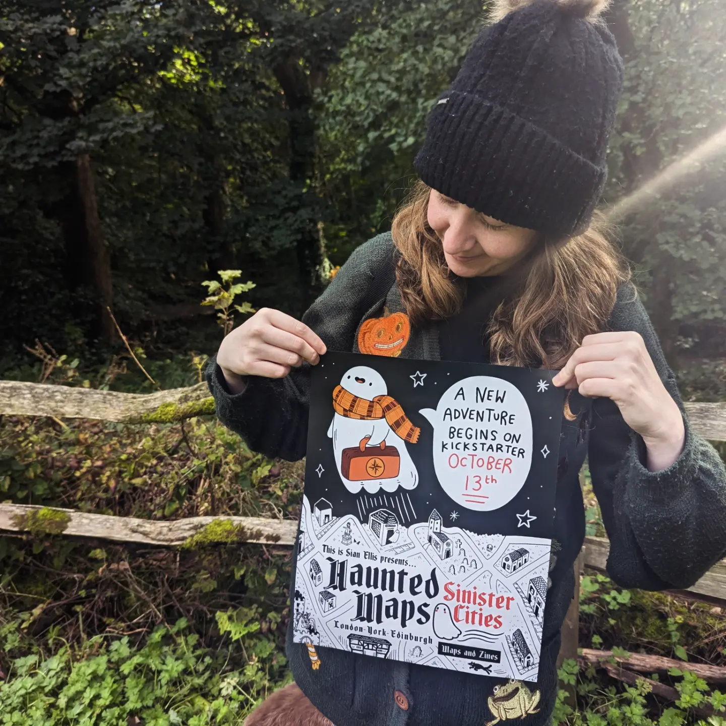 Sian Ellis holding her Haunted Maps prints in the woods